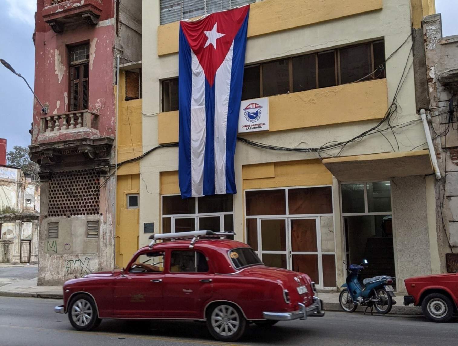 Red classic car in front of building adorned with Cuban flag